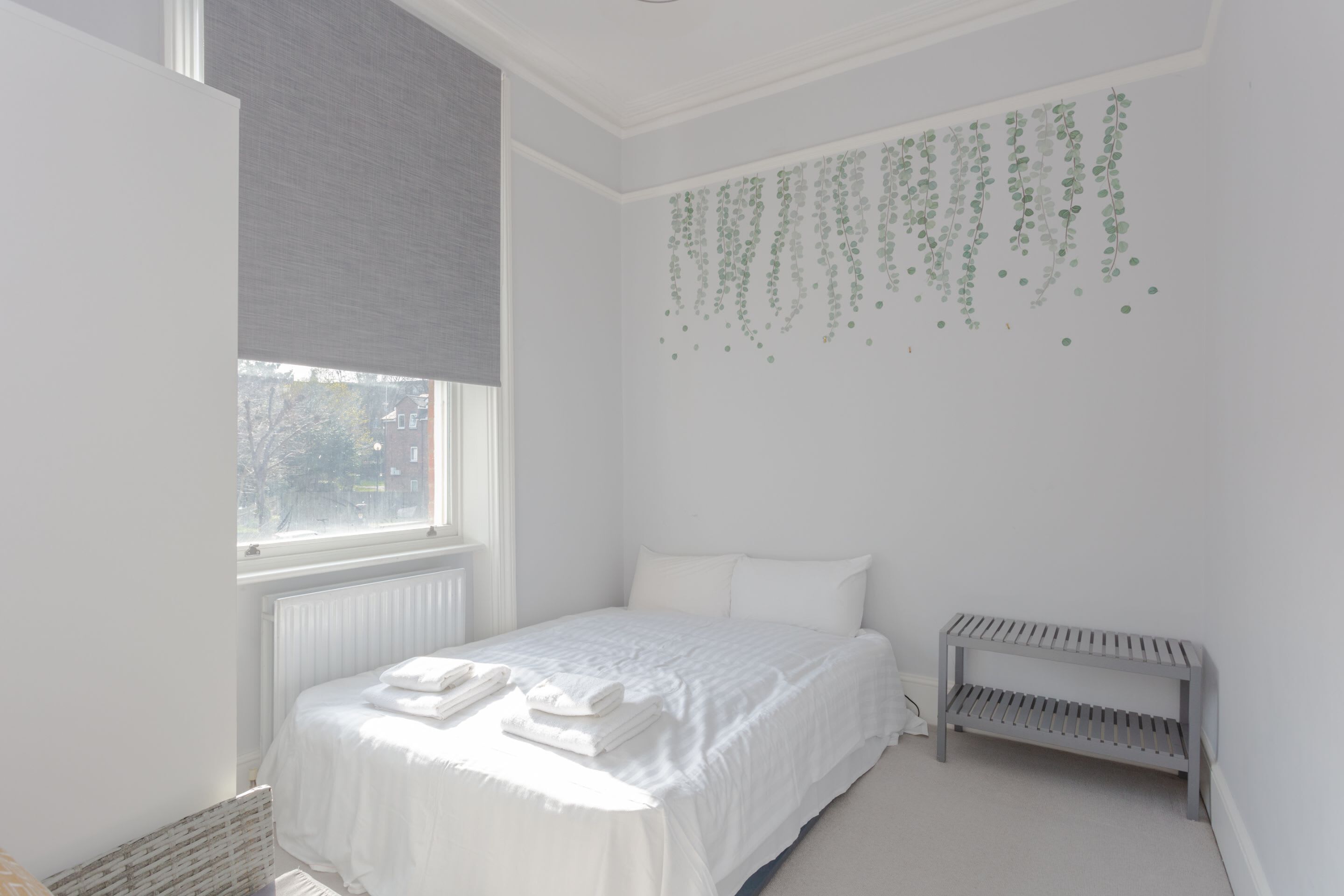 Ein Schlafzimmer mit Bett, Heizkörper, Fenster und einer Bank.