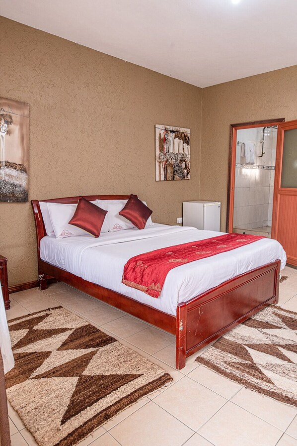 A bedroom with a wooden bed, white bedding, a red throw blanket, and a patterned rug.