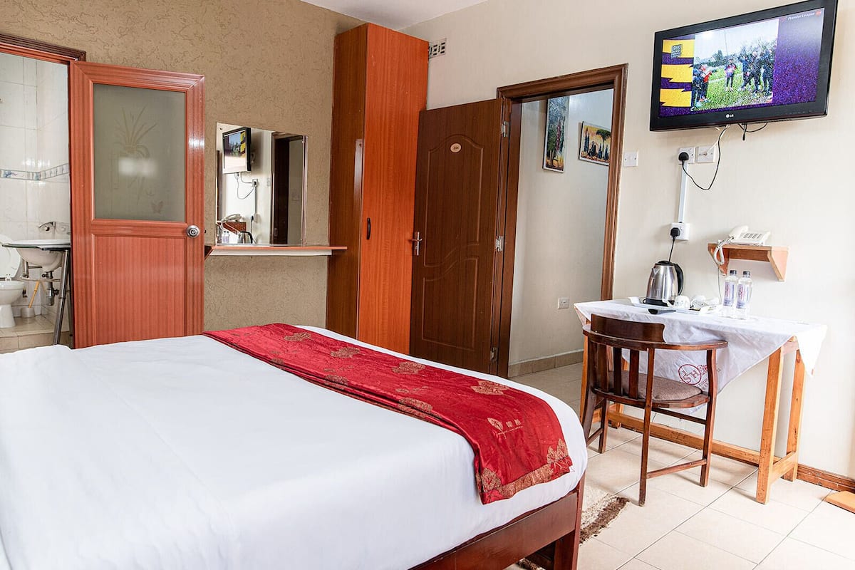 A hotel room with a bed, a desk with a chair, a television, and a bathroom visible through an open door.