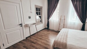 A bedroom with a wooden floor, a bed with a white bedspread, a window with curtains, and a door. - La Luna Otel Cunda (Ayvalik)