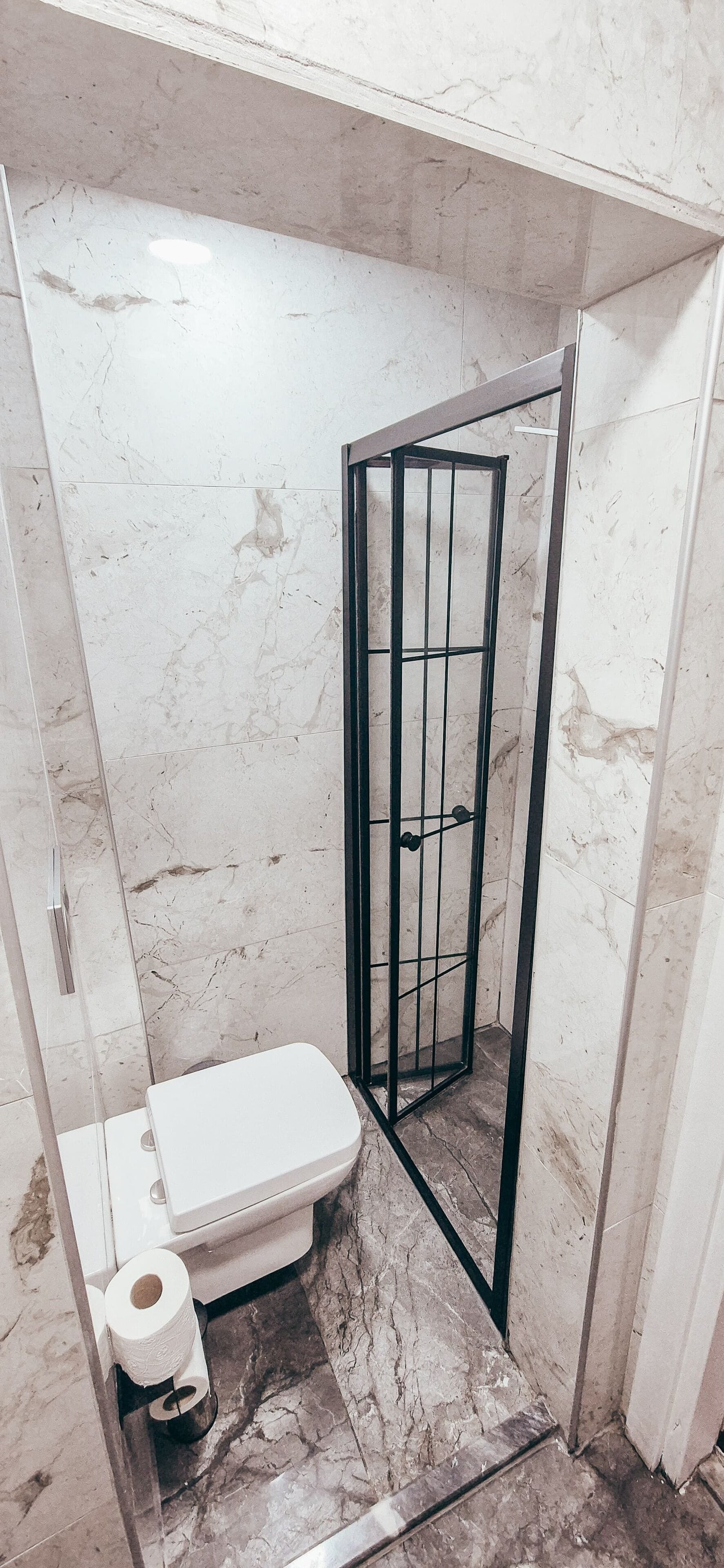 A bathroom with a toilet, a shower enclosure, and a marble floor.