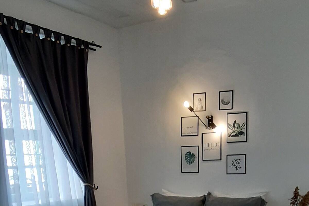 A bedroom with a bed, a bedside table, a wall-mounted light, and framed artwork.