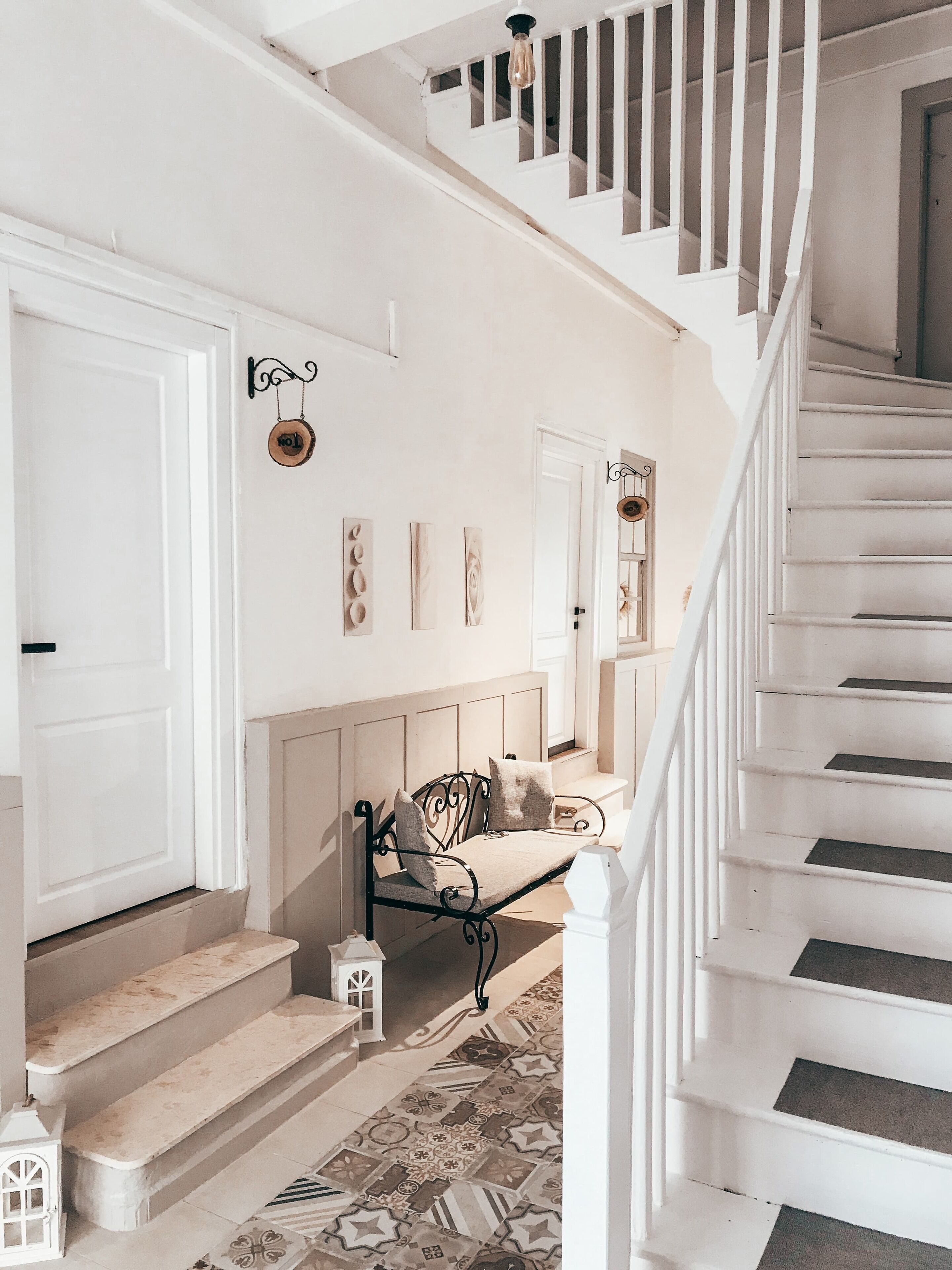 A staircase with white railings and a patterned carpet leading to a landing with a bench and wall-mounted decor.
