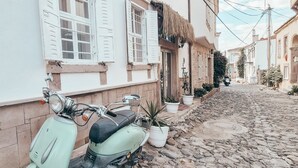 A narrow cobblestone street with a vintage scooter parked against a building with white shutters and a thatched roof. - La Luna Otel Cunda (Ayvalik)