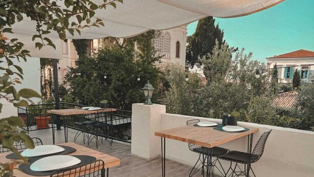An outdoor patio area with tables and chairs, surrounded by greenery and a building in the background. - La Luna Otel Cunda (Ayvalik)