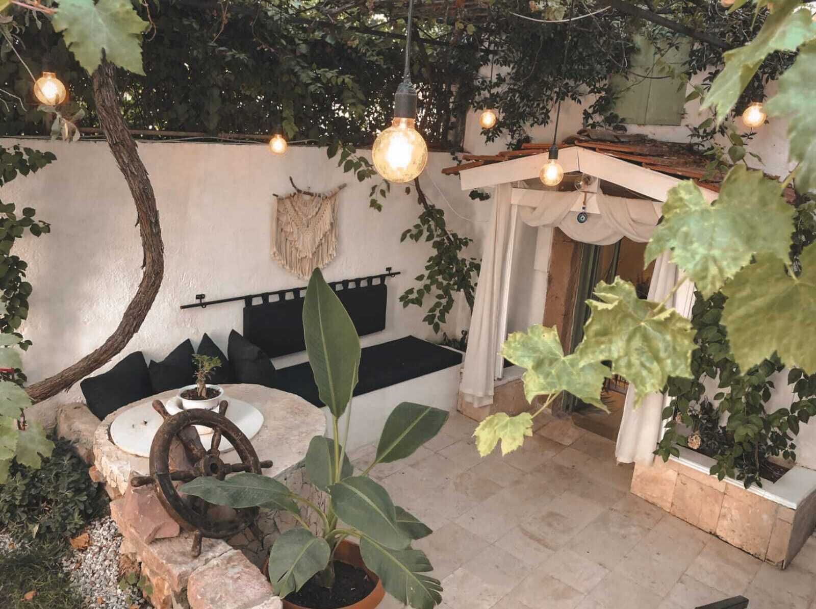 Un espacio al aire libre acogedor con un banco de piedra rústico, una rueda antigua y lámparas colgantes.