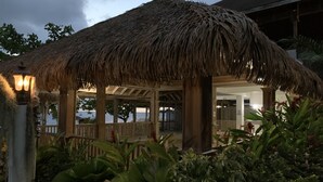 A thatched-roof structure with wooden pillars, surrounded by lush greenery. - Comfy Stay In Jamaica -enjoy 7 Miles Of White Sand Beach! 2 Bedroom Villa by RedAwning (Negril)