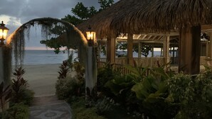 A beachside resort with a thatched-roof structure, a pathway leading to the beach, and a view of the sea. - Comfy Stay In Jamaica -enjoy 7 Miles Of White Sand Beach! 2 Bedroom Villa by RedAwning (Negril)