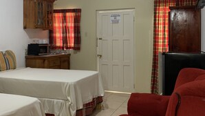 A room with two beds, a red sofa, a wooden cabinet, a microwave, and a television. - Comfy Stay In Jamaica -enjoy 7 Miles Of White Sand Beach! 2 Bedroom Villa by RedAwning (Negril)
