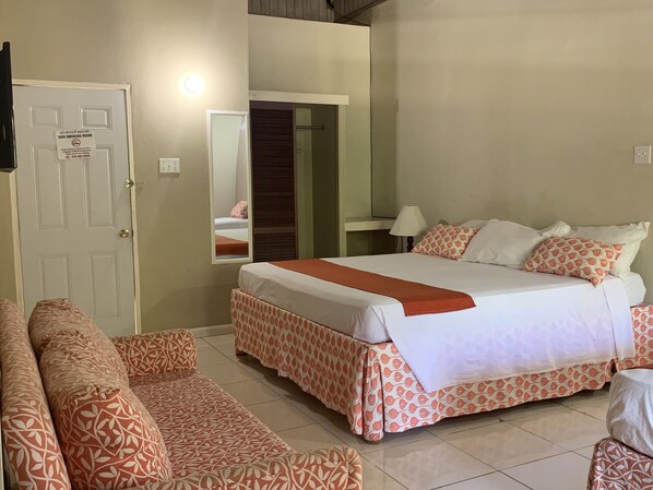 A hotel room with a bed, a sofa, a mirror, and a non-smoking sign on the door.