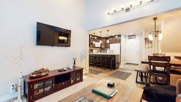 Una sala de estar moderna con un televisor de pantalla plana, un mueble de madera para entretenimiento y una zona de comedor con mesa y sillas.