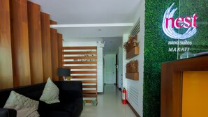 Eine moderne Hotellobby mit einer schwarzen Couch, Holzelementen, einem Empfangstresen und einer grünen Wand mit einem Logo.
