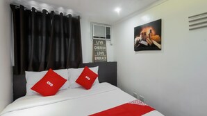 Ein ordentlich bezogenes Bett mit weißer und roter Bettwäsche, ein schwarzer Vorhang, eine Wand-Klimaanlage und ein motivierendes Poster.