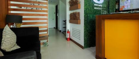 A hotel reception area with a wooden slatted wall, a reception desk, and a green wall with a logo.
