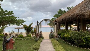 A pathway leading to a beach with a thatched-roof structure and lush greenery.