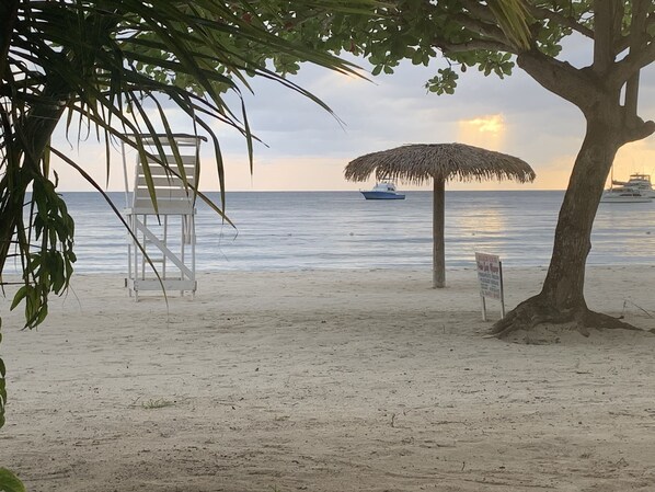 Una playa con una sombrilla de paja, una silla de madera y un cartel.