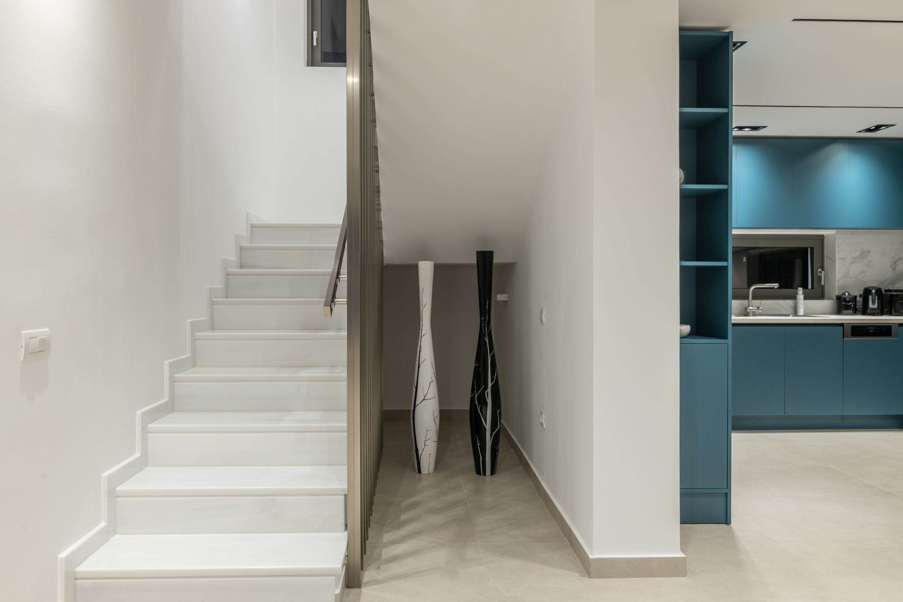 A staircase leading to a modern kitchen with teal cabinetry and white countertops.