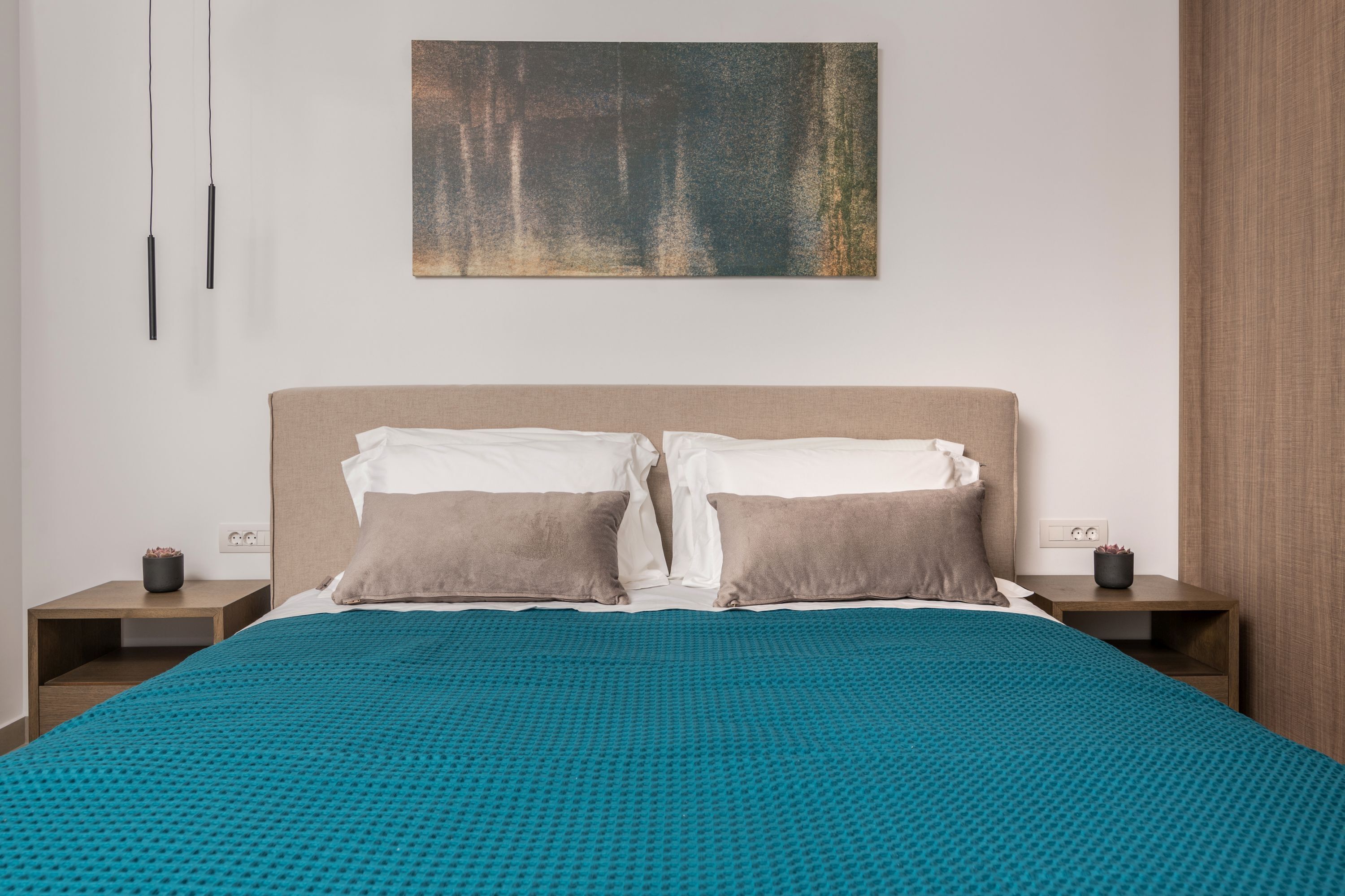 A modern bedroom with a large bed, two bedside tables, a wall-mounted artwork, and a nightstand with a lamp.