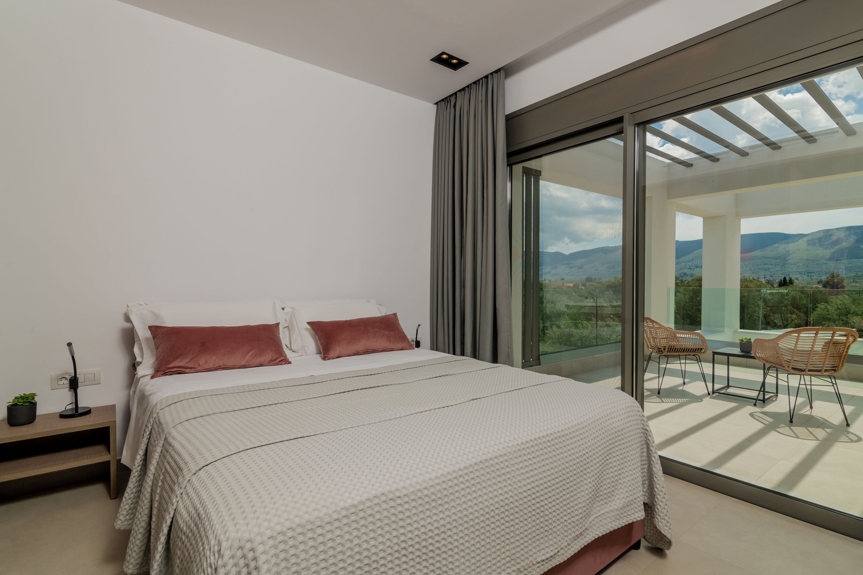 Un dormitorio moderno con una cama grande, una mesita de noche y vistas al exterior a través de un ventanal corredero.