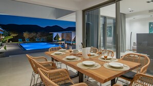 Comedor con vista a la piscina, sillas de mimbre y una mesa de madera dispuesta para seis personas.