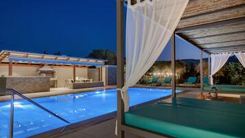 A swimming pool with a covered area and lounge chairs, surrounded by a building with a tiled roof and outdoor seating.