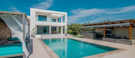 A modern house with a swimming pool, outdoor seating, and a covered patio.