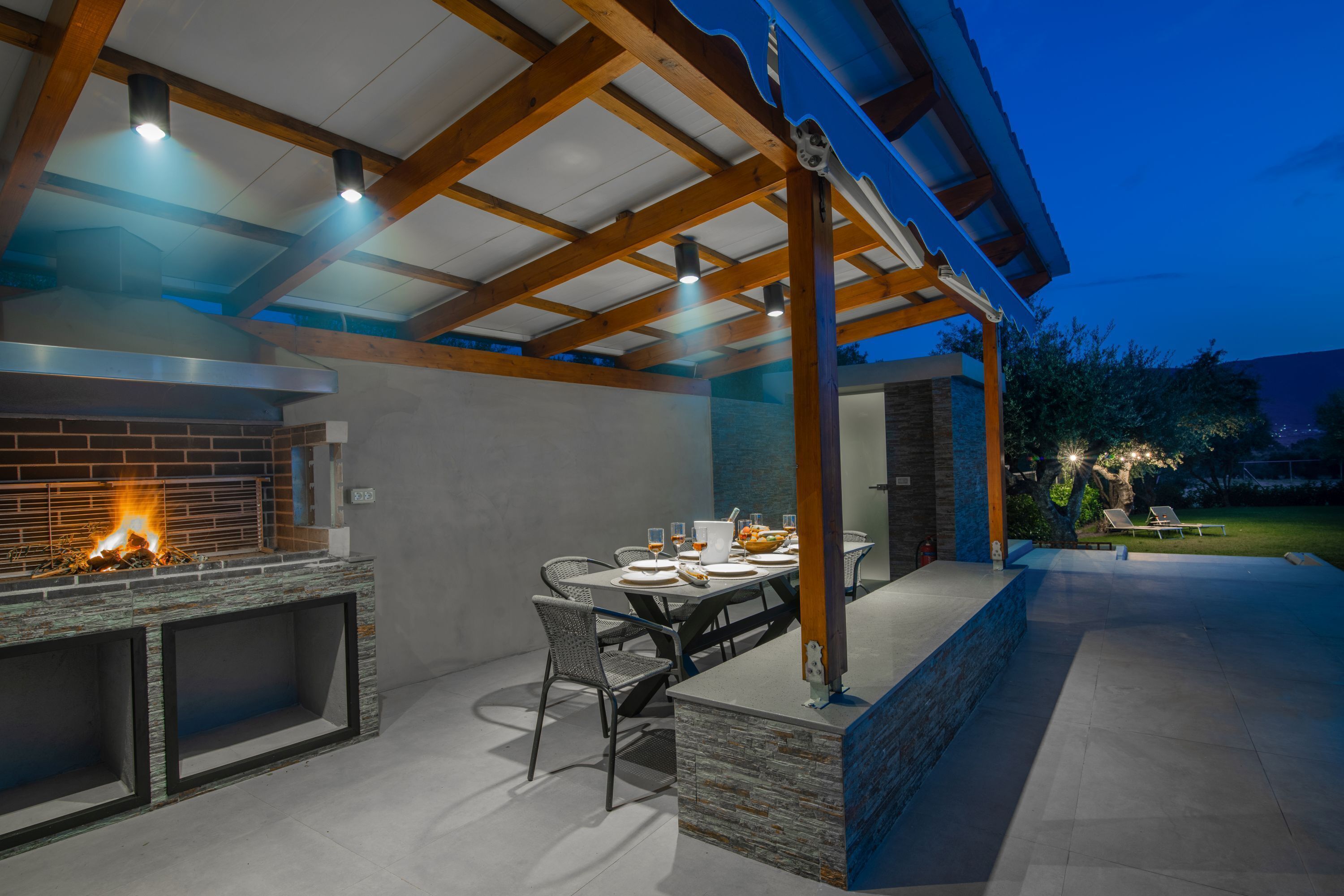 Une terrasse extérieure avec une cheminée en briques, une table à manger pour quatre personnes et un espace salon abrité.