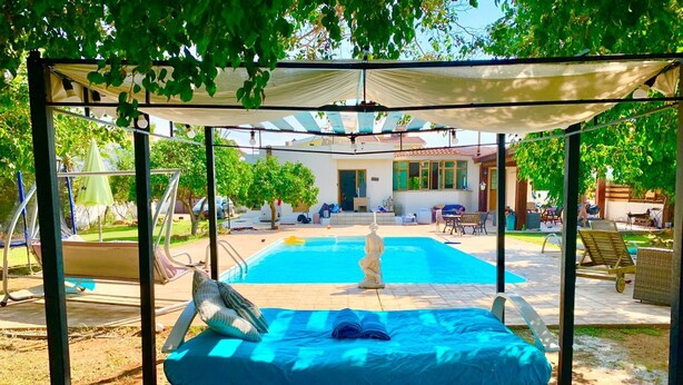 A poolside area with a covered seating area, a statue, and a view of a building in the background. - Remarkable 2-bed Villa in Protaras (Paralimni)