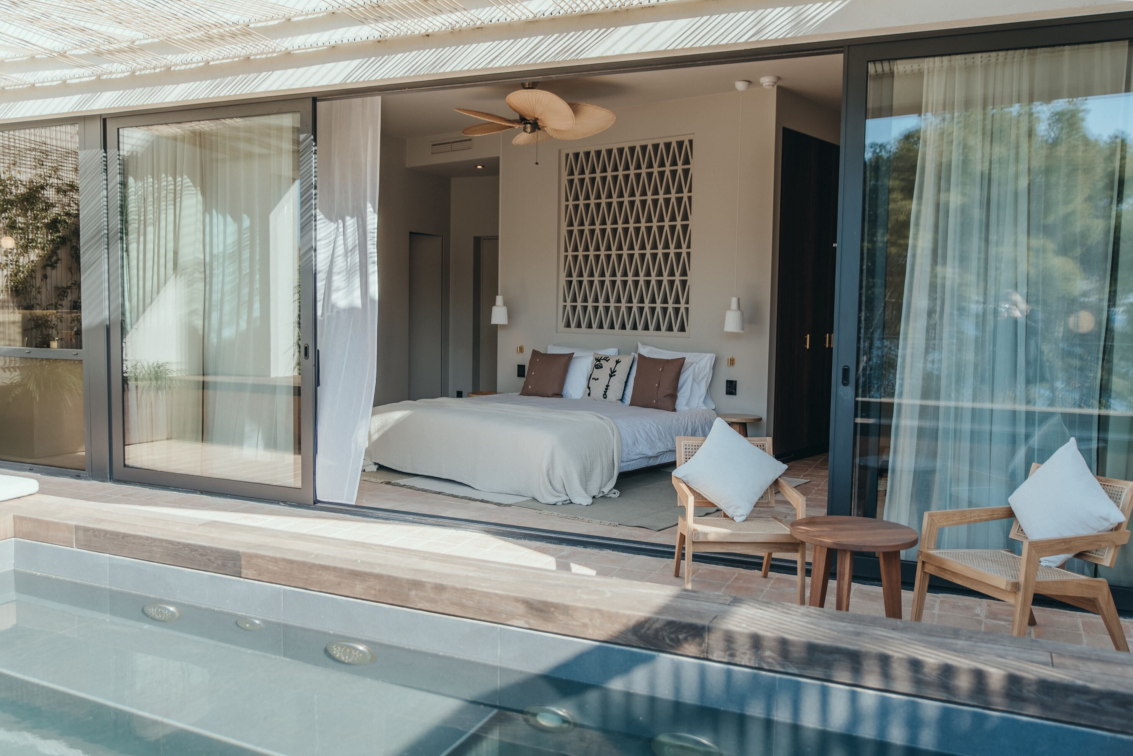 Um quarto moderno com uma cama grande, portas de vidro deslizantes que dão para uma varanda com piscina e um ventilador de teto.