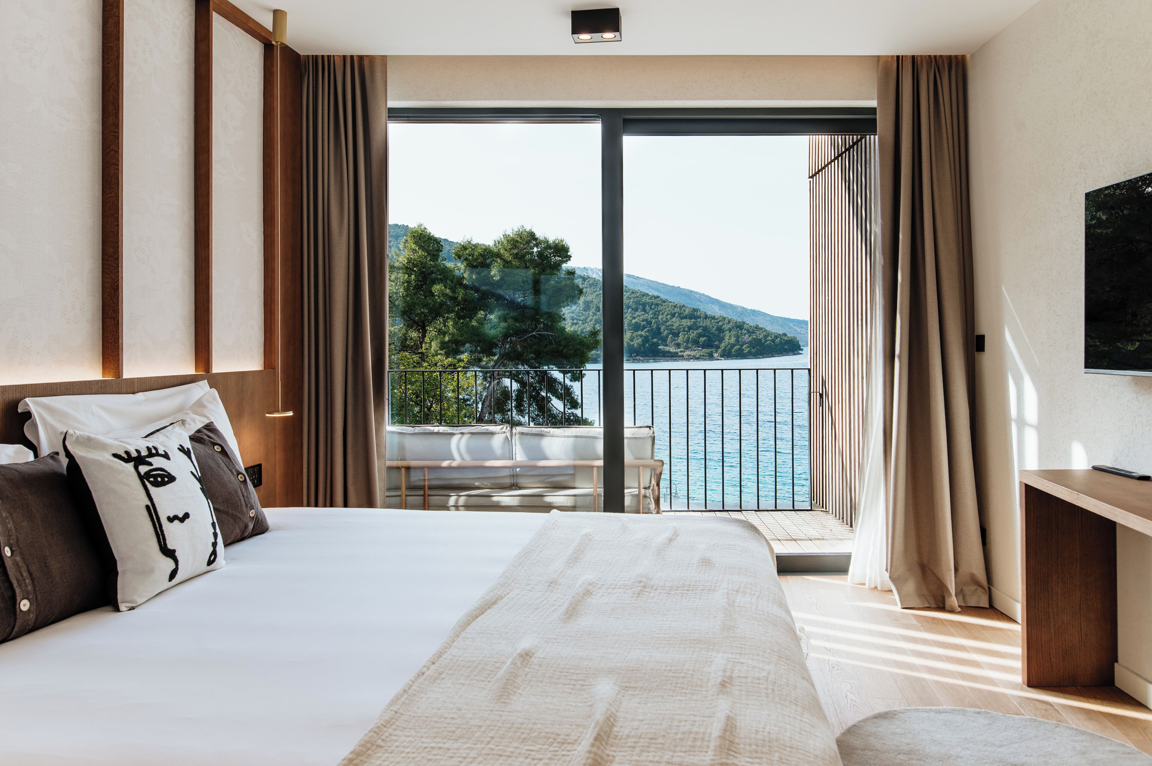 Een slaapkamer met een groot bed, een televisie en een balkon met uitzicht op zee en heuvels.