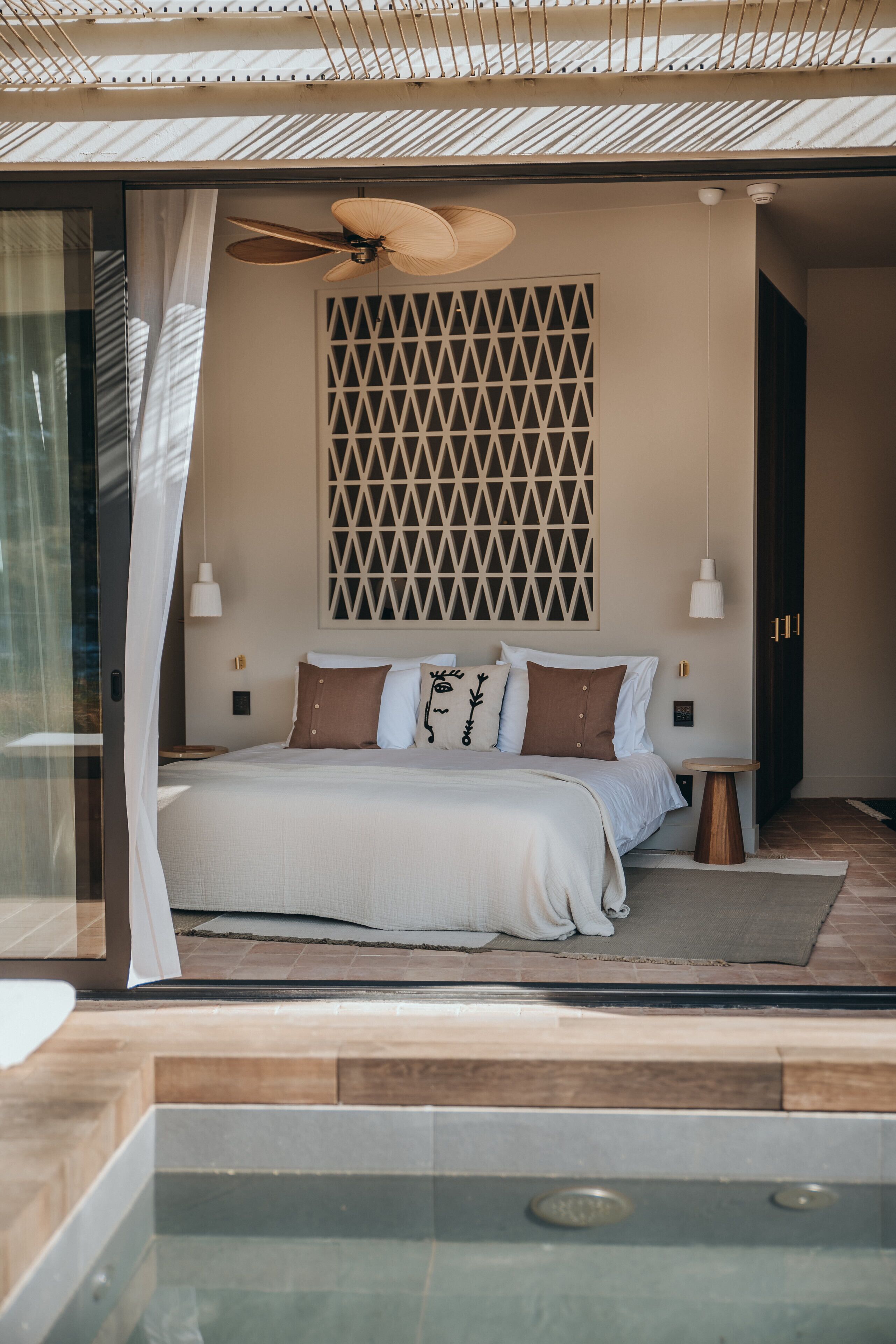 A modern bedroom with a large bed, a ceiling fan, and a geometric wall design.