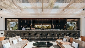 Un área de estar exterior moderna con barra, sofás acolchados y una mesa redonda.