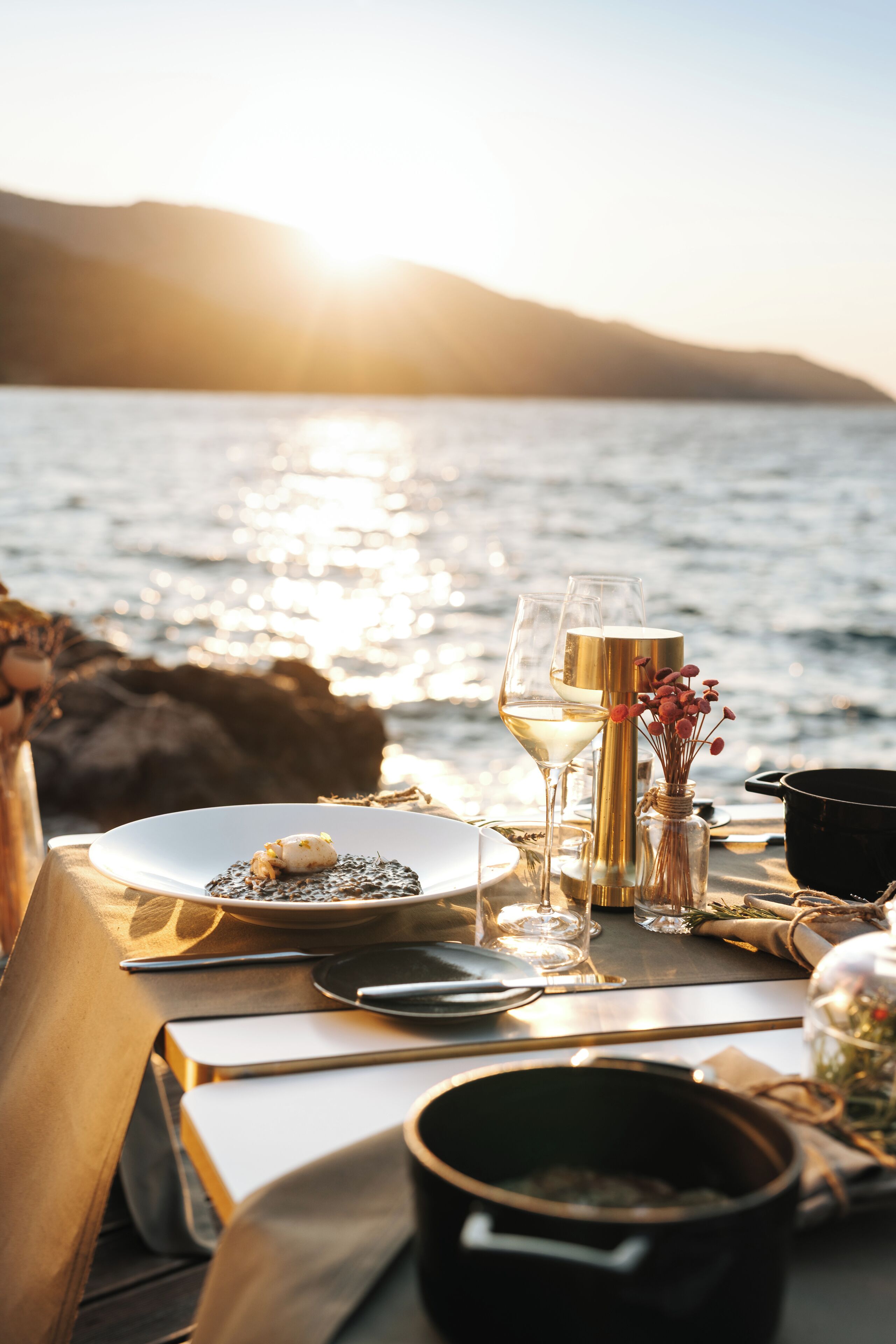 Une table dressée pour un repas, avec une vue sur la mer et une montagne en arrière-plan.