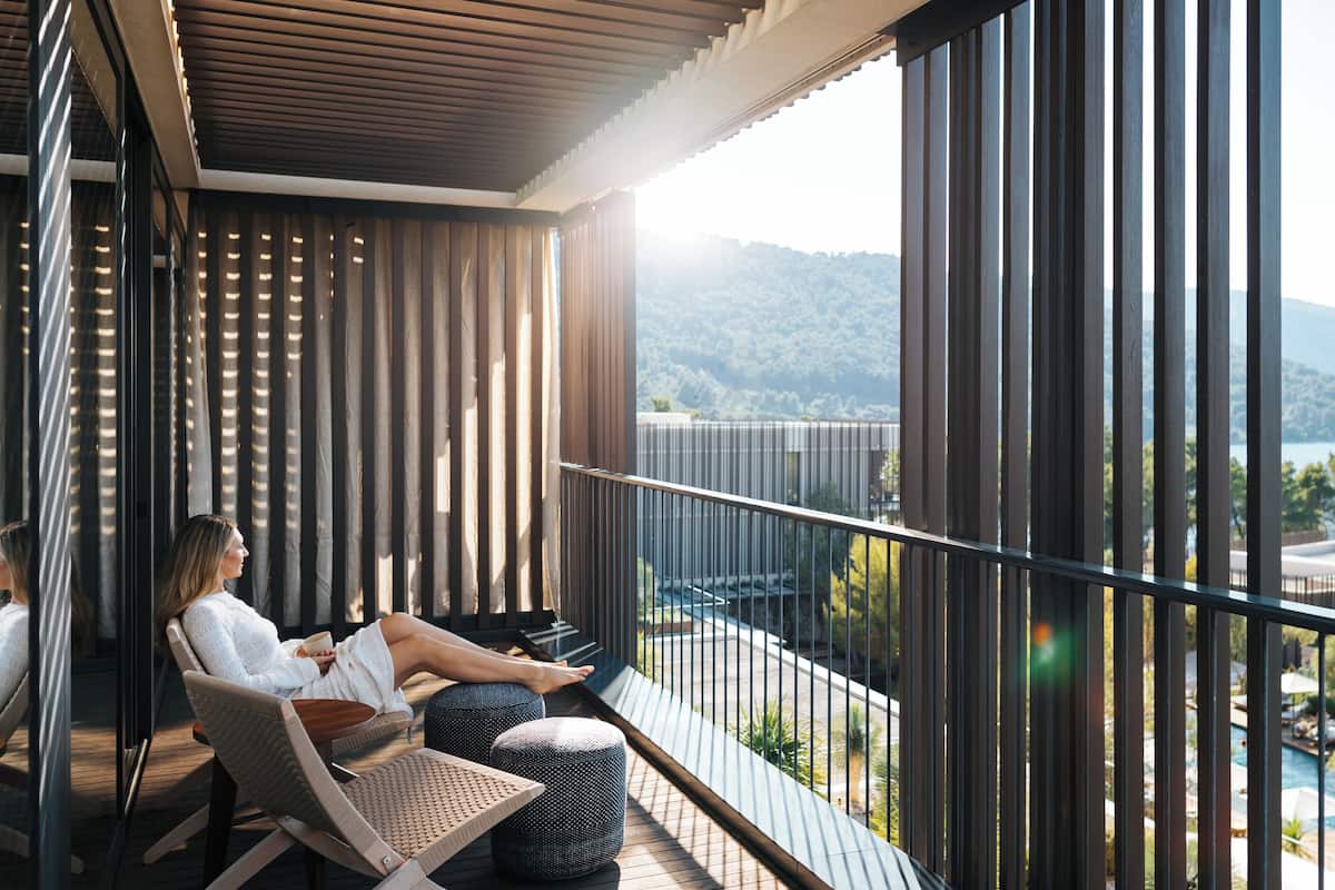 A balcony with a view of a lake and mountains, featuring a seating area with a table and chairs.