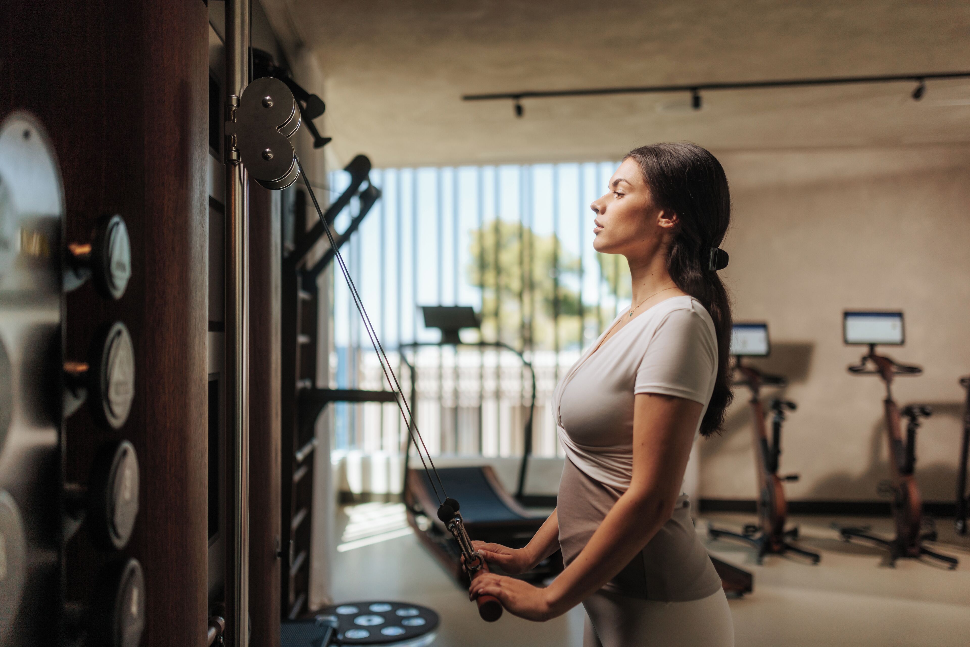 Ein Fitnessstudio mit Trainingsgeräten, darunter ein Kabelzuggerät und Laufbänder.