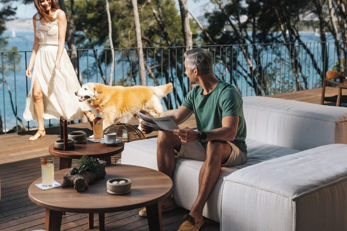 A deck with a sofa and a table, a woman in a white dress, and a dog.