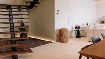 A modern interior with a wooden staircase, a white door, a round woven basket, and a white sofa with black chairs.