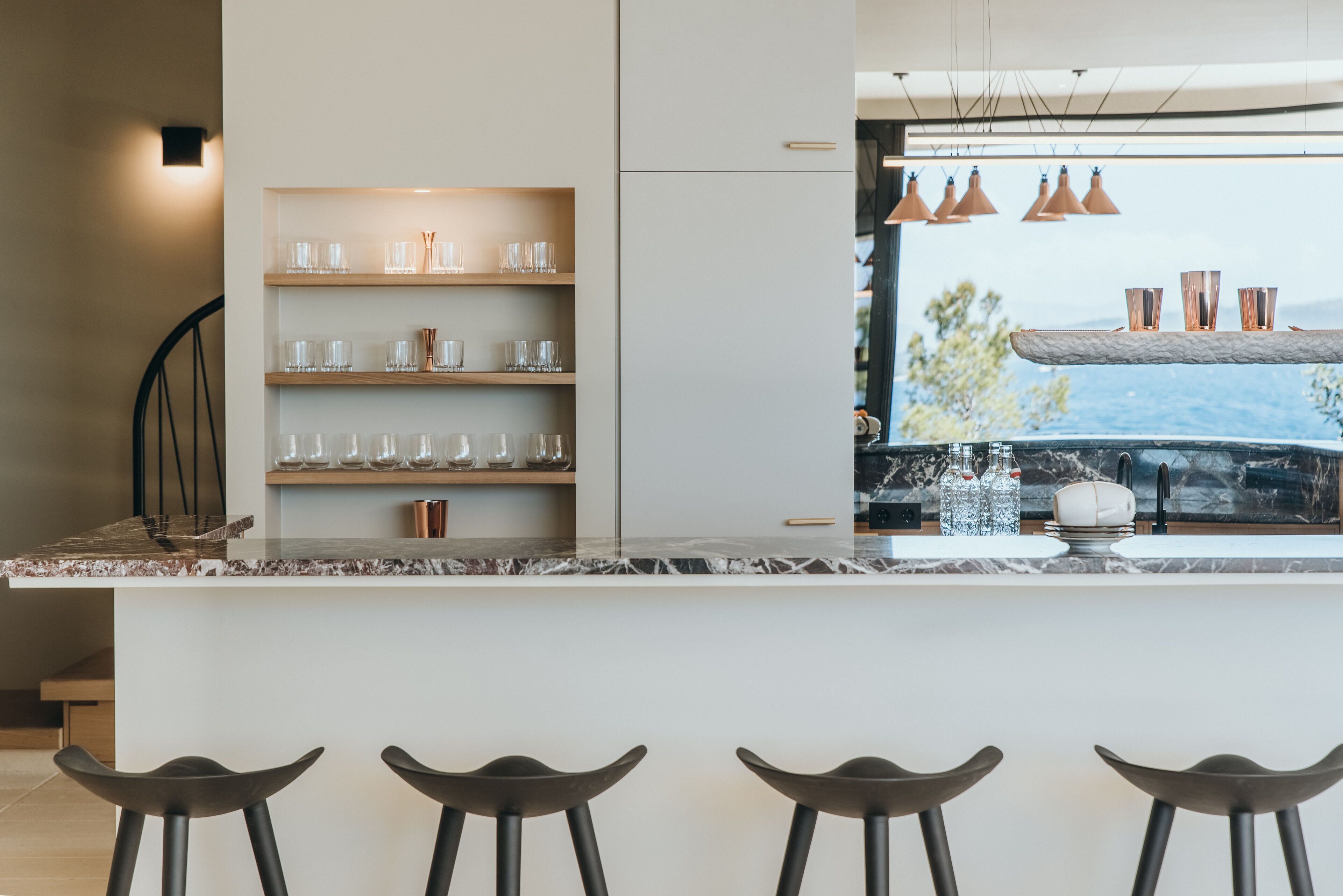 A modern kitchen with a marble countertop, built-in shelves, and a bar area with stools.