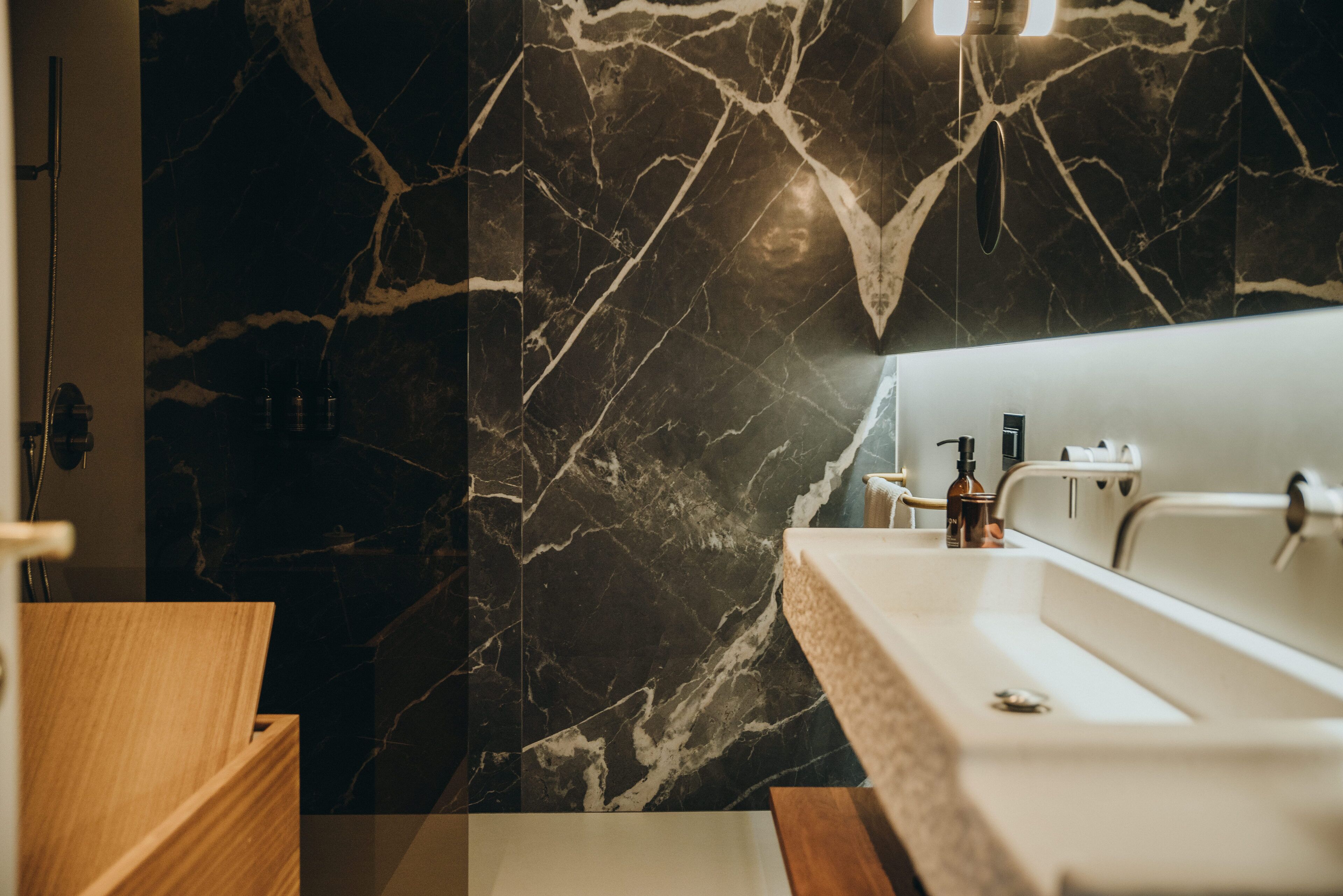 Ein modernes Badezimmer mit Marmorwand, Waschtisch aus Holz und weißem Waschbecken.
