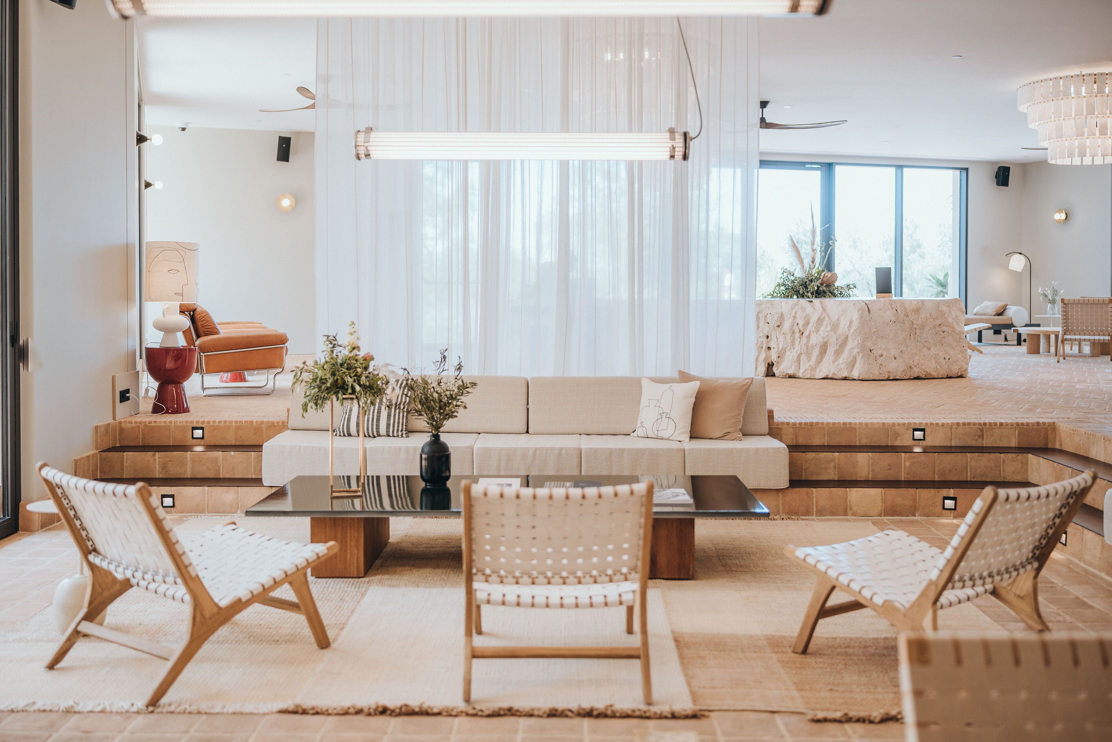 A modern living room with a sofa, two wicker chairs, a coffee table, and a large window with sheer curtains.