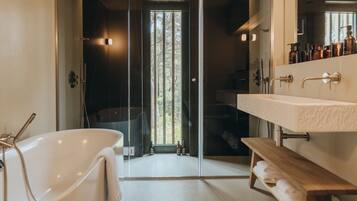 A modern bathroom with a freestanding bathtub, a large mirror, and a wooden shelf with towels.