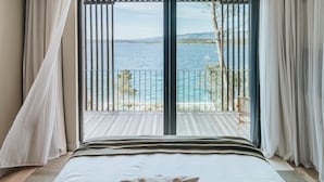 Un dormitorio con una cama grande, ropa de cama blanca y vistas al mar a través de un balcón con barandilla de metal.