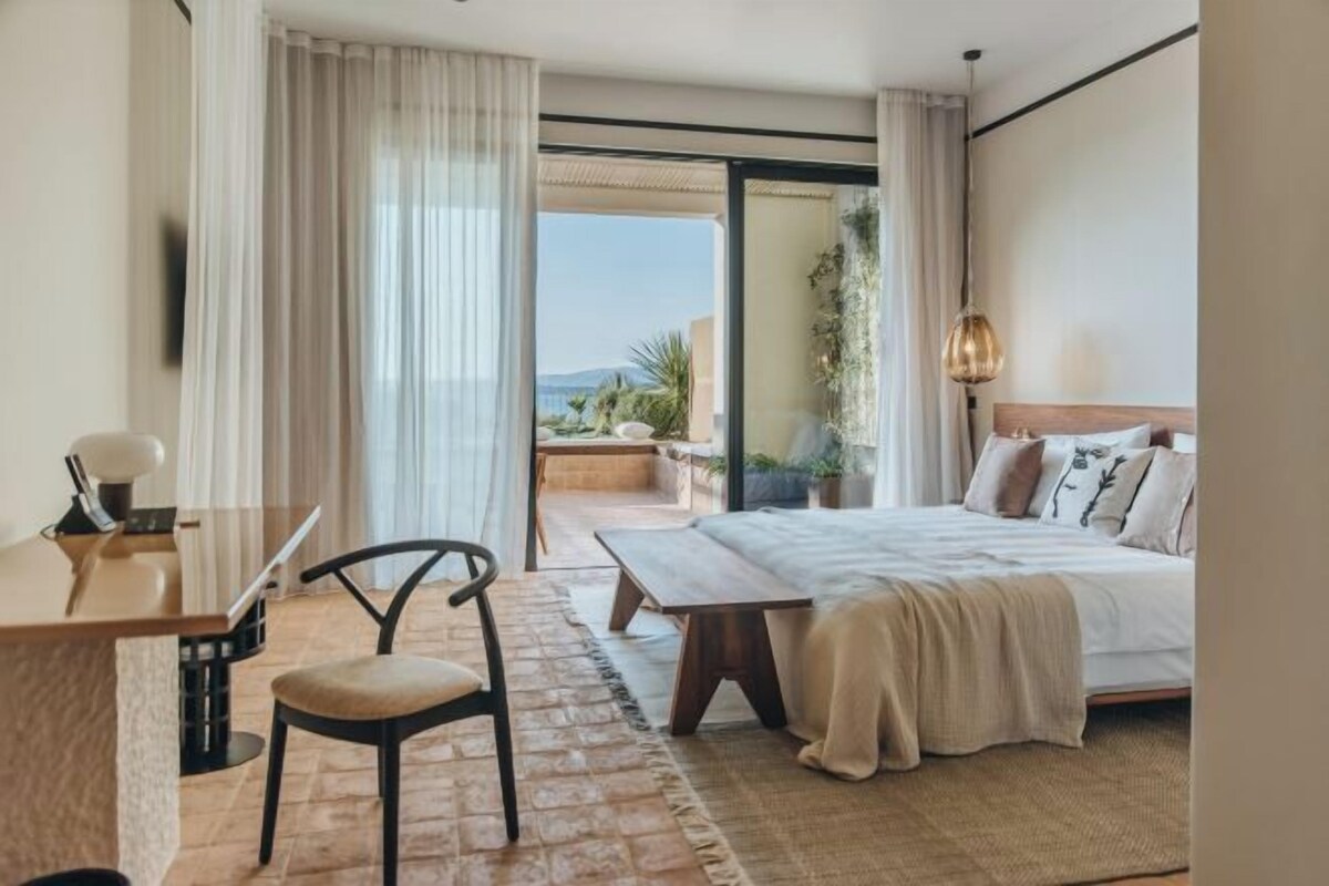 A hotel room with a bed, a desk, a chair, and a view of the outdoors.