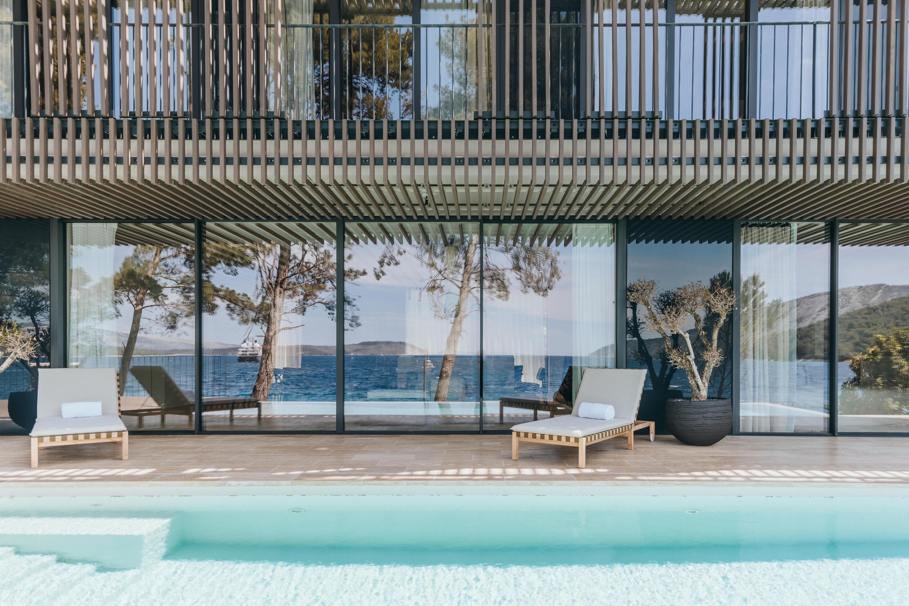 A modern outdoor pool area with two lounge chairs and a large window overlooking the sea.