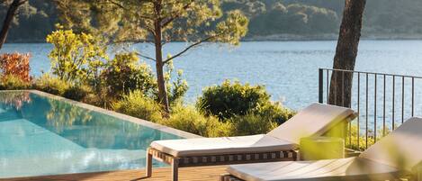 Terraza de madera con sillones de descanso y una piscina con vistas a un lago.
