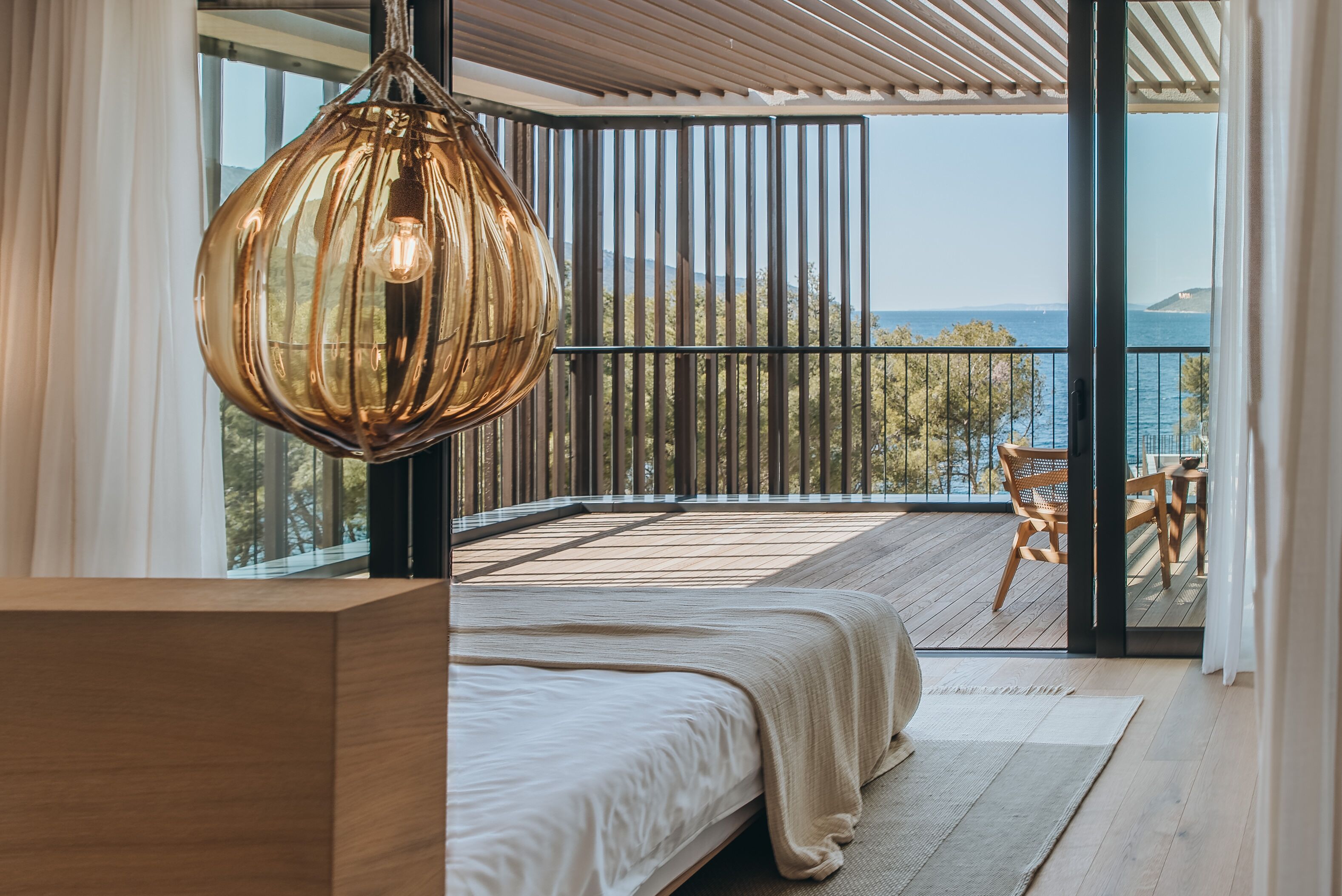 Un dormitorio con una cama grande, una lámpara colgante y vistas al mar desde un balcón.