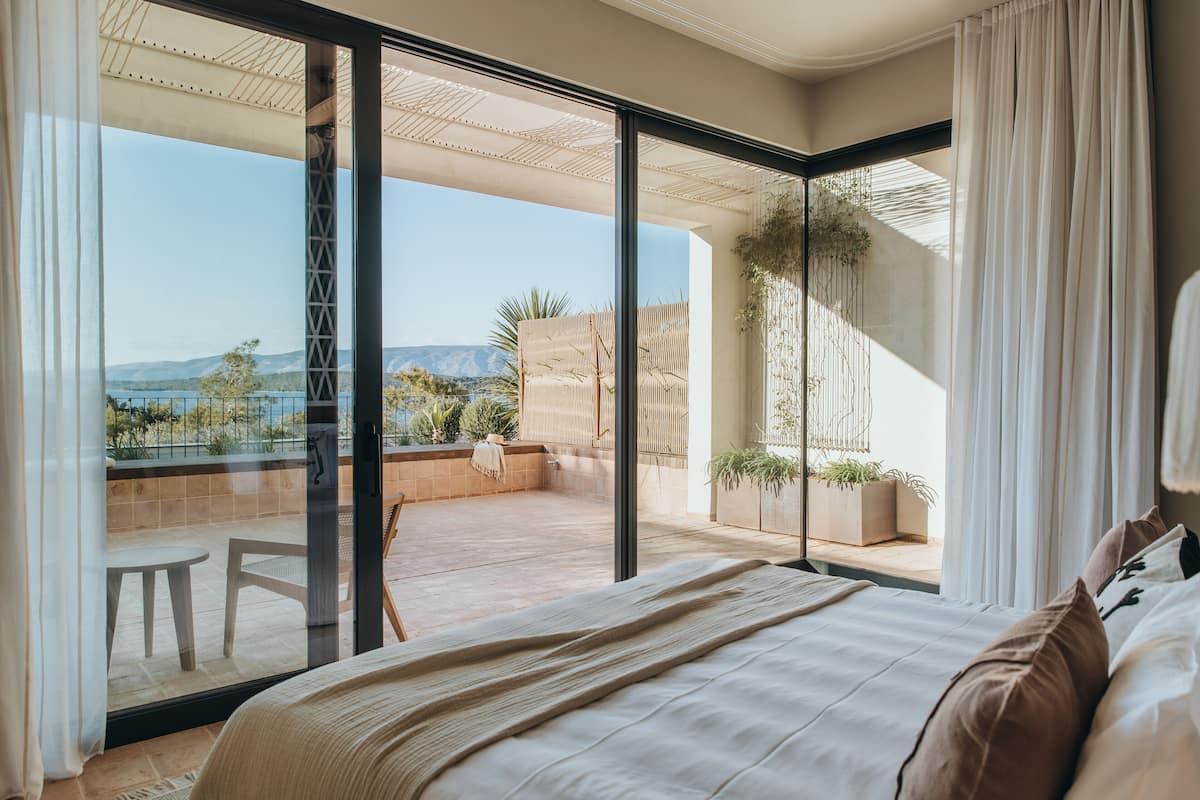 A bedroom with a large sliding glass door leading to a balcony with a view of the mountains.