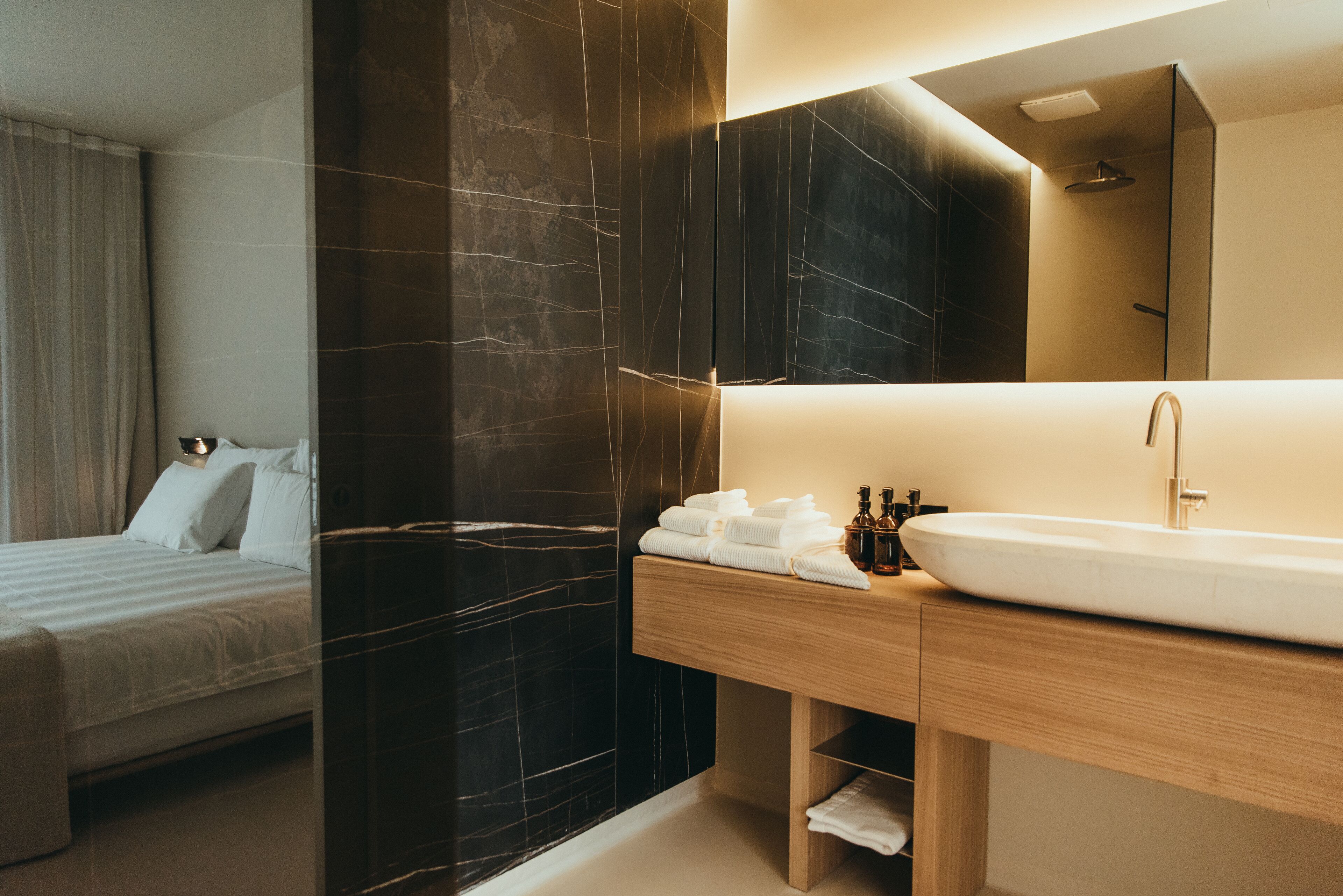 A modern hotel room with a large bed, a wooden vanity with a sink, and a dark marble accent wall.