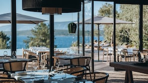 Un área de comedor al aire libre con mesas y sillas, sombrillas grandes y vistas al mar.