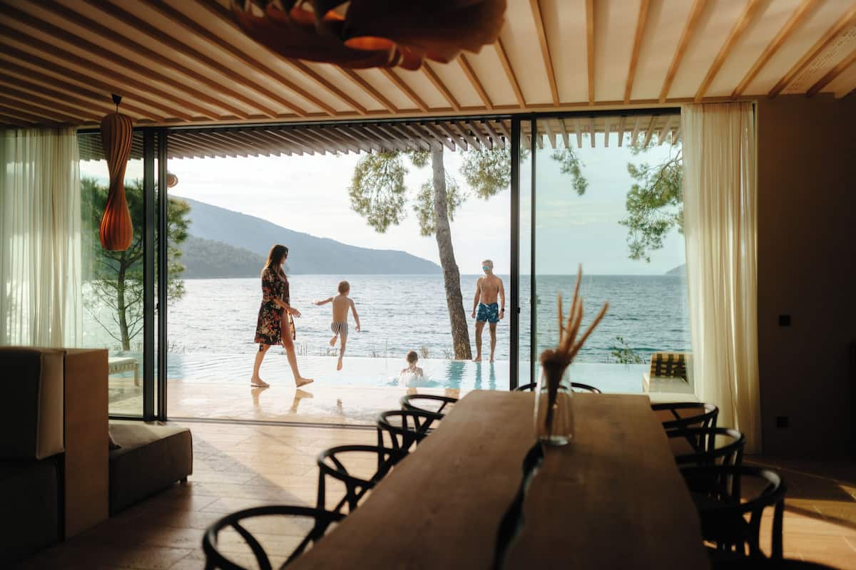 A modern interior with a large wooden table and chairs, a view of a swimming pool, and a glass door leading to the outdoors.